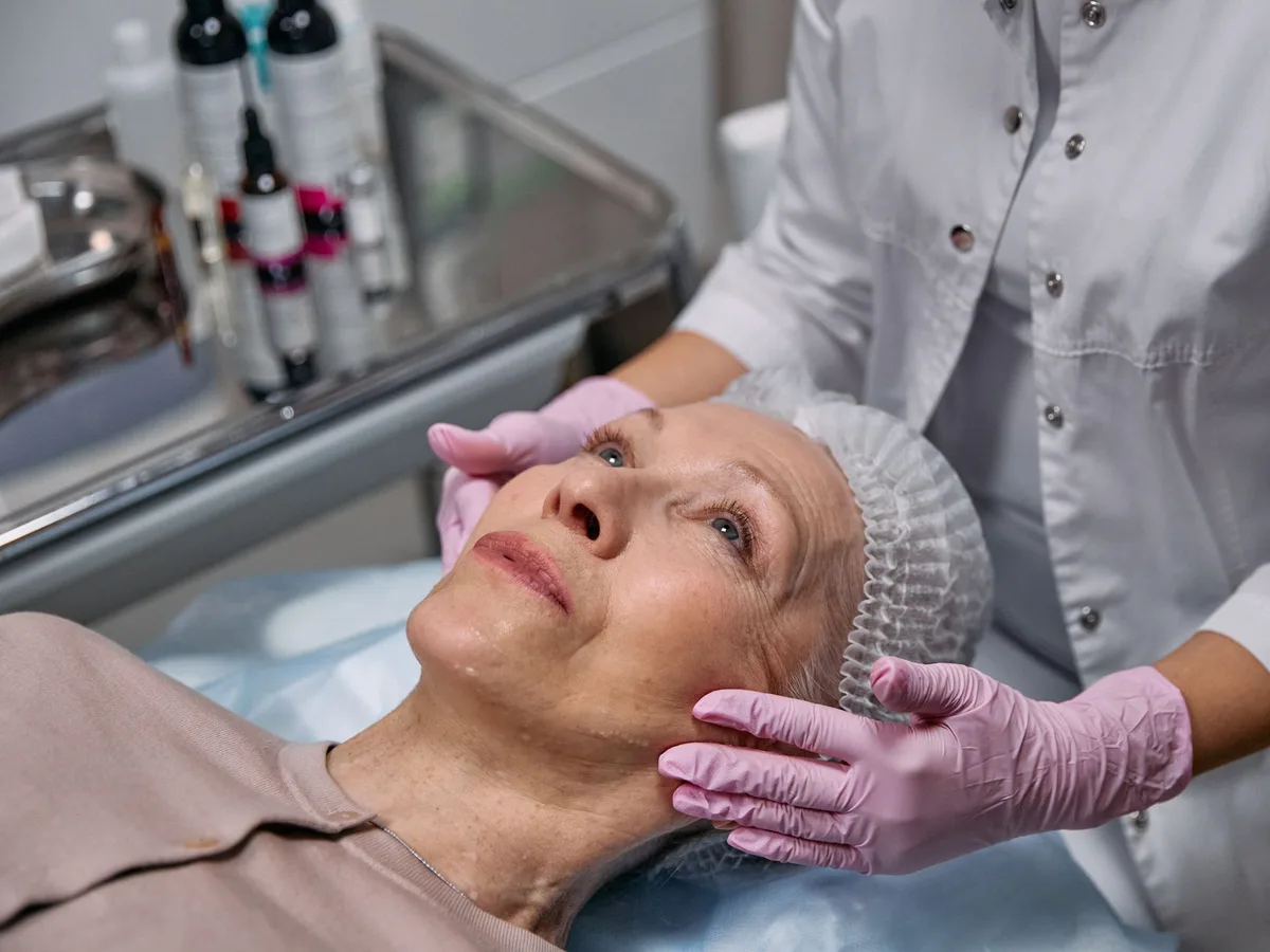 Mature woman receiving a facial treatment from a gloved skin professional
