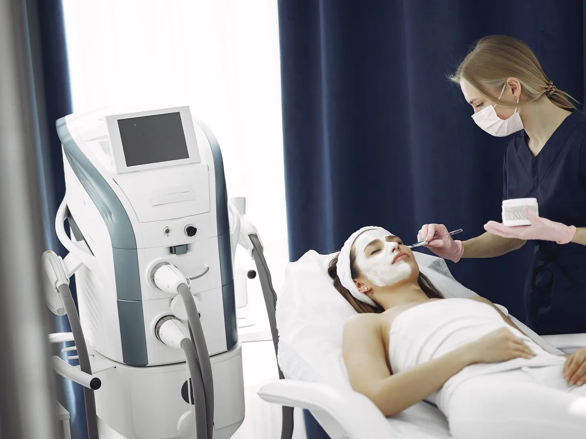 Aesthetic laser platform with a screen and handpieces beside a treatment couch